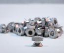 A collection of silver-colored 5/16 inch breakaway nuts scattered on a light background.